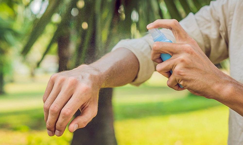 A person spraying insect repellent on their arm outdoors to protect against mosquito bites.