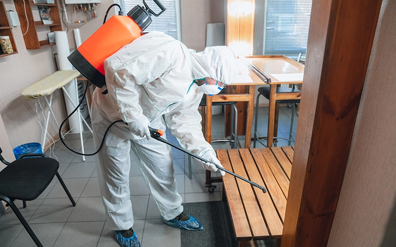 disinfector in a protective suit and mask sprays disinfectants in the house