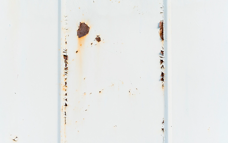 Close-up of a white metal surface with patches of rust and peeling paint.