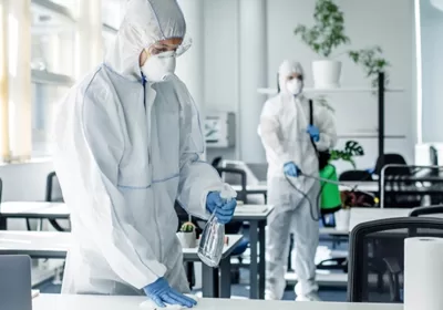 Professionals in protective suits disinfecting an office space, highlighting pest prevention and sanitation measures in commercial buildings.